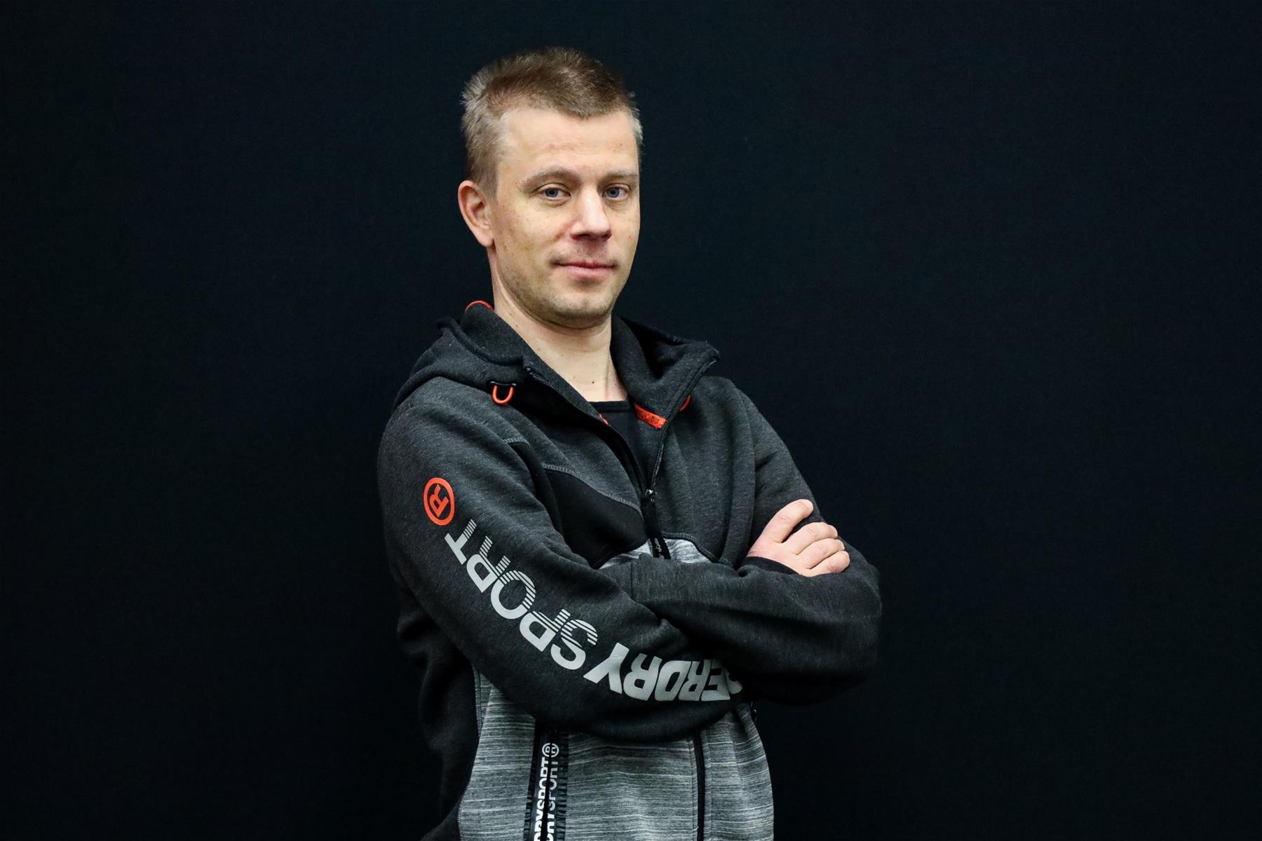 Antti Silvennoinen seisoo mustaa taustaa vasten kädet ristissä ja katsoo kameraan.